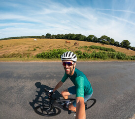 Cyclist taking selfie while cycling on country road with horses grazing in background