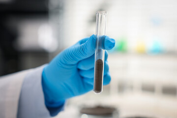 Scientist with test tube of soil sample in laboratory, closeup
