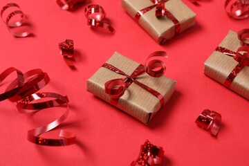Shiny serpentine streamers and gift boxes on red background, above view