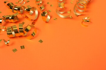 Shiny party streamers and confetti on orange background, closeup. Space for text