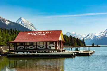 Fototapeta premium Scenic view of Maligne Lake boathouse in Jasper National Park, Canada. Calm waters, snow-capped mountains, and forest reflect pristine wilderness and tranquility.