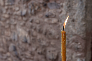 a narrow lit prayer candle with melted wax dripping from it