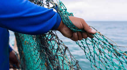 Fisherman’s hand gripping tangled green fishing nets aboard a boat at sea, representing traditional coastal labor.