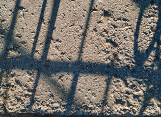Cinder and gravel in the form of small gray stones and the shadow of a fence lattice, viewed from...