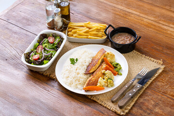 Prato Executivo Brasileiro Peixe filé de tilápia com Arroz, Batata Palha, feijão e Salada em Mesa de Madeira