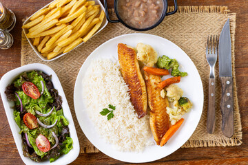 Prato Executivo Brasileiro Peixe filé de tilápia com Arroz, Batata Palha, feijão e Salada em Mesa de Madeira