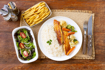 Prato Executivo Brasileiro Peixe filé de tilápia com Arroz, Batata Palha, feijão e Salada em Mesa de Madeira