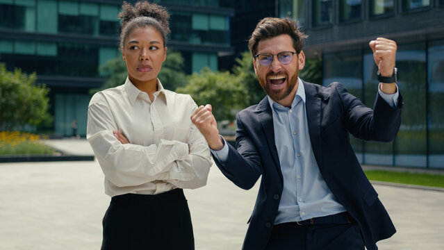 Two multiracial business colleagues different emotions in city African American woman businesswoman girl female upset disappointed failure Caucasian man businessman guy male win yell celebrate victory