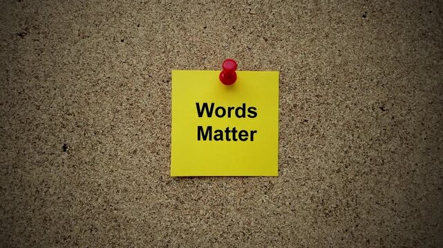 A yellow paper note with the phrase Words Matter on it pinned to a cork board. Close up.