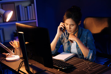 Young beautiful Asian creative woman calling on phone desk to customer or coworker explaining creator project's high profit while searching market analysis on pc at neon office at night. Stratagem.