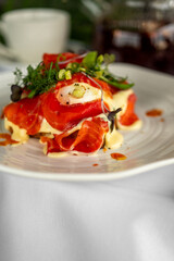Gourmet dish with smoked salmon, poached egg, and fresh greens, elegantly plated and garnished with herbs on a white plate. Top view, bright and appetizing.