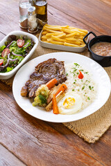 Prato Executivo Brasileiro de bisteca de boi com Arroz, Batata Palha, feijão, farofa e Salada em Mesa de Madeira
