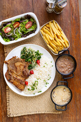 Prato Executivo Brasileiro bisteca de porco com Arroz, Batata Palha, feijão, farofa e Salada em Mesa de Madeira