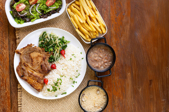Prato Executivo Brasileiro bisteca de porco com Arroz, Batata Palha, feij&atilde;o, farofa e Salada em Mesa de Madeira