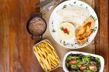 Prato Executivo Brasileiro filé de frango com Arroz, Batata Palha, feijão e Salada em Mesa de Madeira