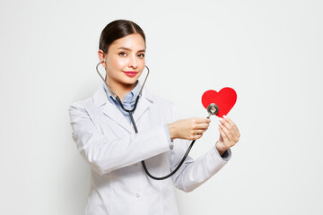 Young female doctor cardiologist with stethoscope over neck showing heart symbol isolated on white...