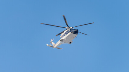 Large white and blue helicopter is soaring through the clear blue sky. It is a medical helicopter,...