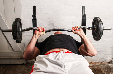 Man doing chest press with barbell lying on bench in home basement gym