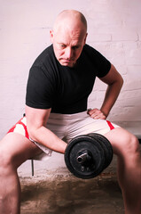 Man lifting black dumbbell for biceps curls sitting in basement home gym