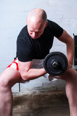 Man working out biceps with dumbbell on bench in home basement gym