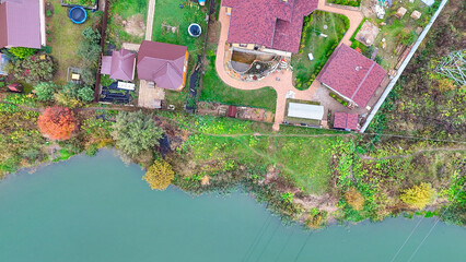House is shown in the background of a green river. The house is surrounded by trees and has a red roof
