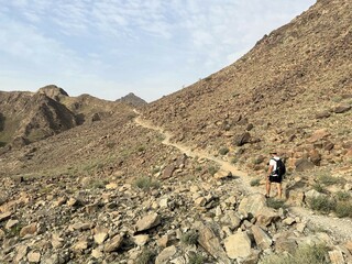 A lone hiker follows a rocky mountain trail near Hatta, UAE. This scene highlights eco-tourism and sustainable travel in the striking, arid landscapes of the Arabian Peninsula.