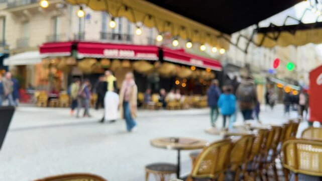 View from restourant on tables and chairs outside and a busy Parisian pedestrian street with restaurants and shops in the trendy Marais district, Paris, France. Out of focus.
