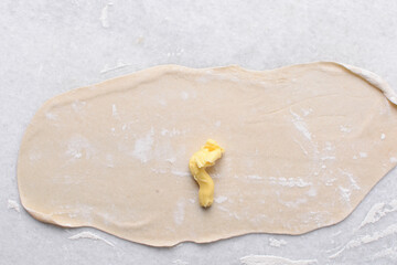 Overhead view of butter being spread on rolled out paratha dough, top view of flaky flatbread dough being covered with ghee, process of making paratha