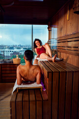 Middle-aged couple in enjoying wellness and heat therapy in wooden sauna.