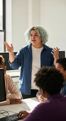 Non-binary teen teaching coding to diverse group in computer lab