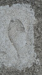 Footprint from a patterned shoe sole on rough cement covered with a layer of white dust, photographed outdoors in daylight, suggesting recent human presence or activity on the site.