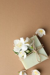 Soap bar and jasmine flowers on light brown background, flat lay. Space for text