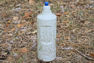 garbage from one dirty old white plastic bottle stands on the gray ground on the street