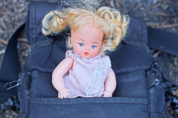 one brown plastic toy doll in a dress with red hair lies in the pocket of a black bag on a summer street