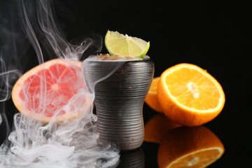 Hookah bowl with smoke and fruits on black table, closeup