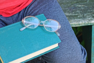 green book and glasses lie on the legs of an old man in gray clothes on a summer street