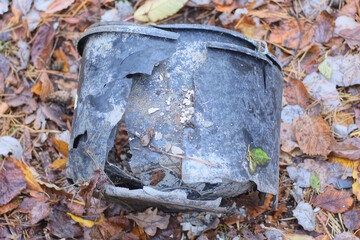garbage from a piece of a broken black plastic bucket stands on the brown ground on the street