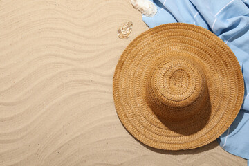Beach towel, straw hat and seashells on sand outdoors, flat lay. Space for text