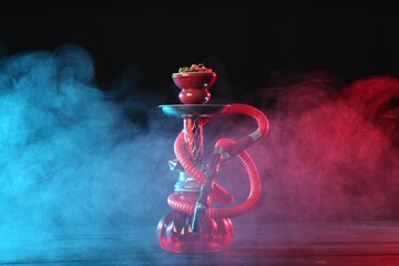 Hookah on wooden table with smoke in color lights against black background