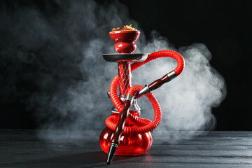 Hookah on wooden table with smoke against black background