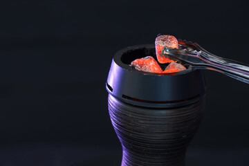 Putting smoldering charcoal cube into hookah holder on dark background, closeup. Space for text
