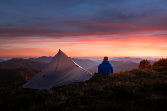 Hiker near his tent against the backdrop of an incredible sunset sky in autumn mountains. Landscape photography
