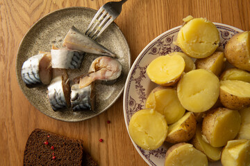 Top view of sliced mackerel and boiled potatoes served on wooden table with rye bread and fork,...