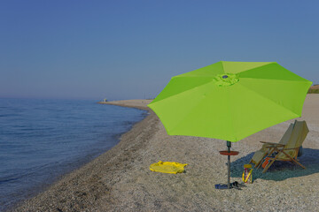 Beach scene with lime green umbrella.Beach scene with lime green umbrella and sun loungers. Pebble...