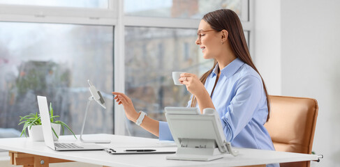 Beautiful secretary working with tablet computer and coffee cup at table in office