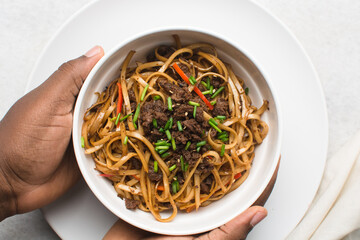 Overhead view of mongolian ground beef noodles in a white bowl, top view of ground beef noodles with scallions, green and red pepper