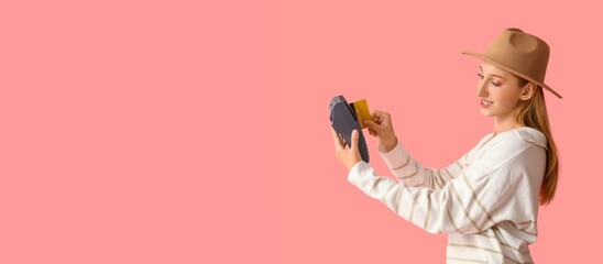 Young woman with payment terminal and credit card on pink background with space for text