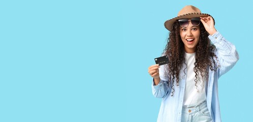 Surprised African-American woman with sunglasses and credit card on blue background with space for...