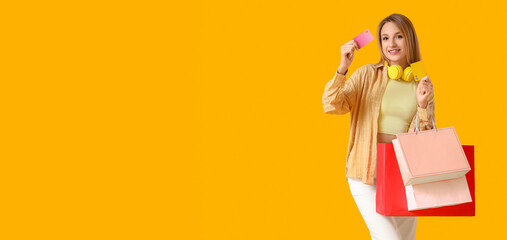 Beautiful young happy woman with headphones, credit cards and shopping bags on yellow background