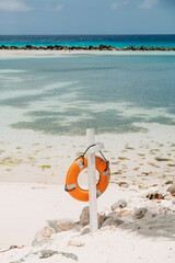 Lifebuoy on a wooden post near a calm beach with clear blue water and soft sand under a sunny sky